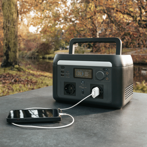 Mestic Power Station MPS-600 beim Laden eines Smartphones auf einem Tisch im Freien beim Camping